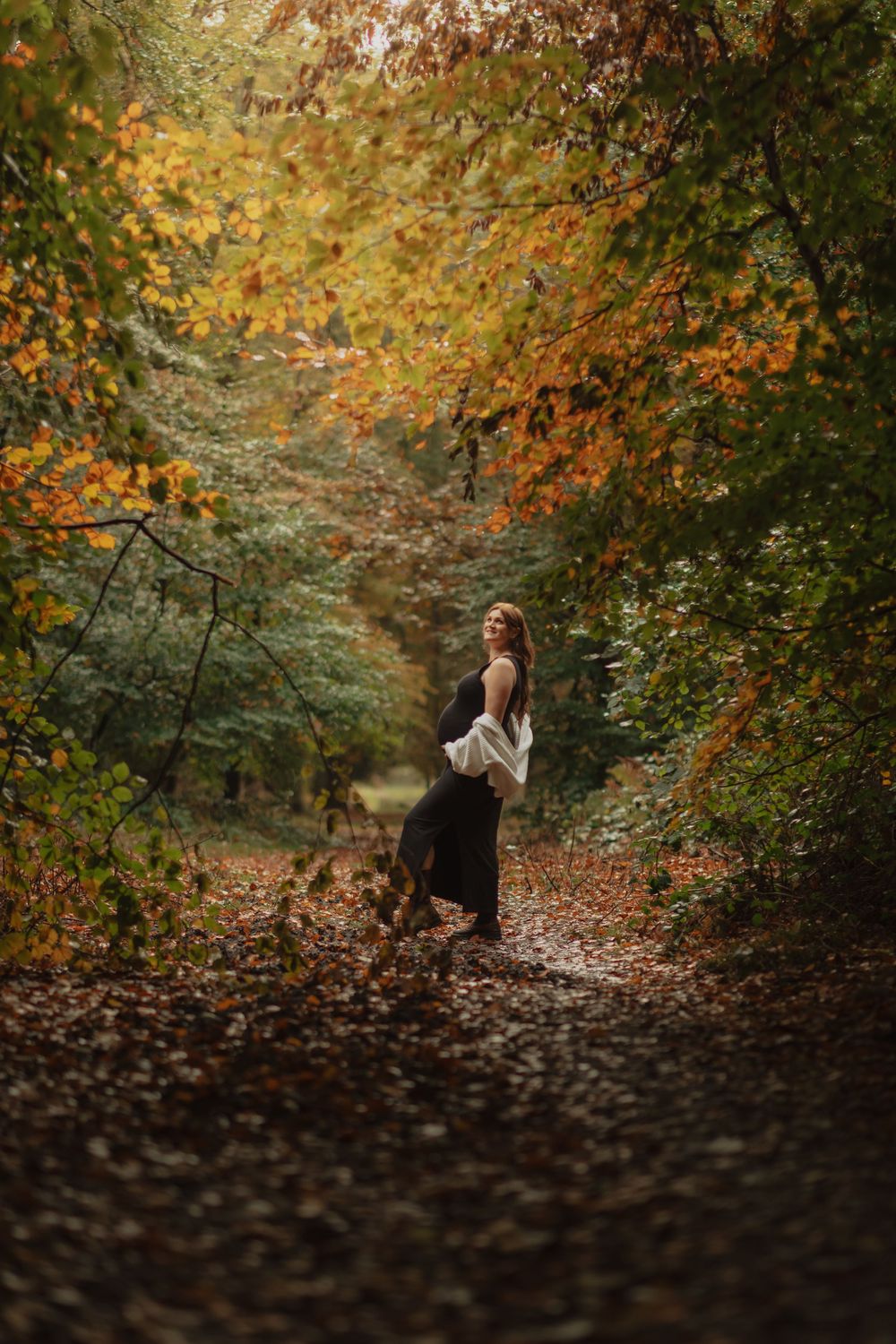 A figure in a long dress walks along a misty forest path surrounded by autumn foliage in warm orange and gold tones.
