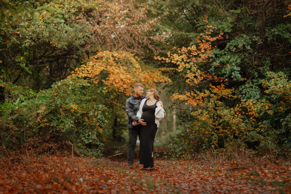 Two people embrace in an autumn forest path surrounded by colorful orange and green foliage.