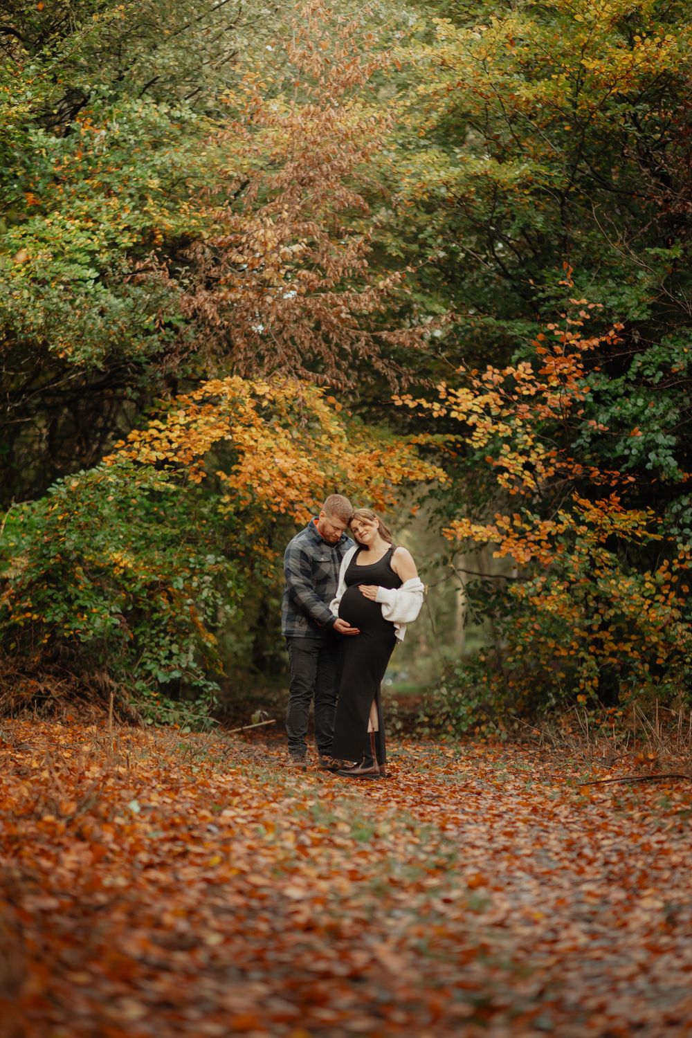 A romantic fall moment on a leaf-covered path surrounded by vibrant autumn foliage in golden and orange hues.