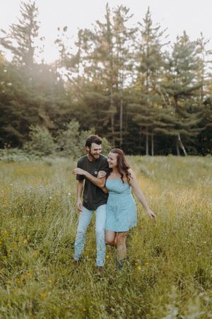 Couple playfully interacting in a wildflower meadow with evergreen trees in the background.