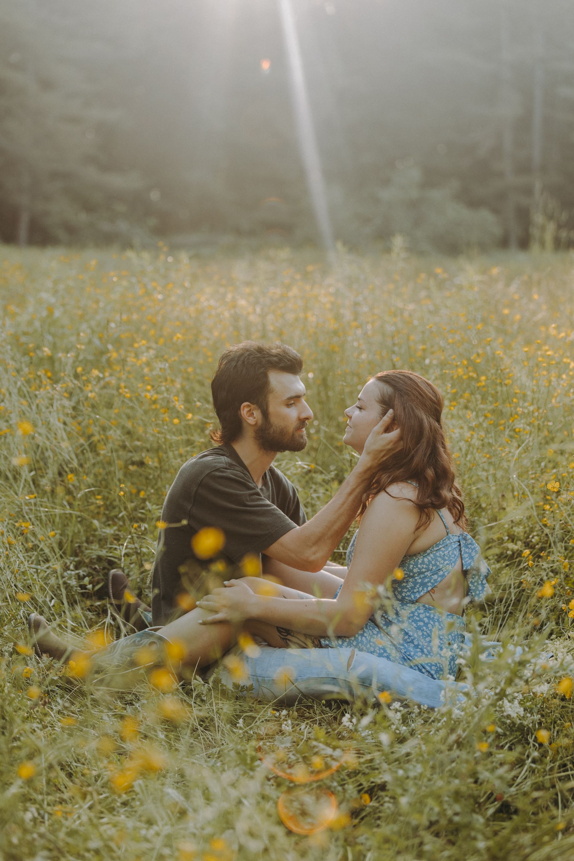 Couple relaxing in tall grass surrounded by yellow wildflowers on a sunny afternoon.