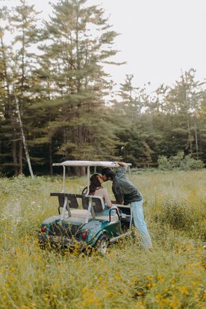 People exploring a turquoise golf cart in a field of yellow wildflowers near a forest.