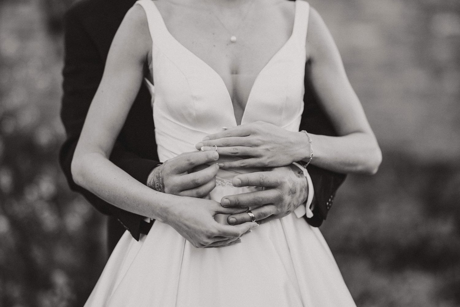 Black and white photo of a couple's embrace during a wedding, with focus on their interlocked hands and white bridal dress.
