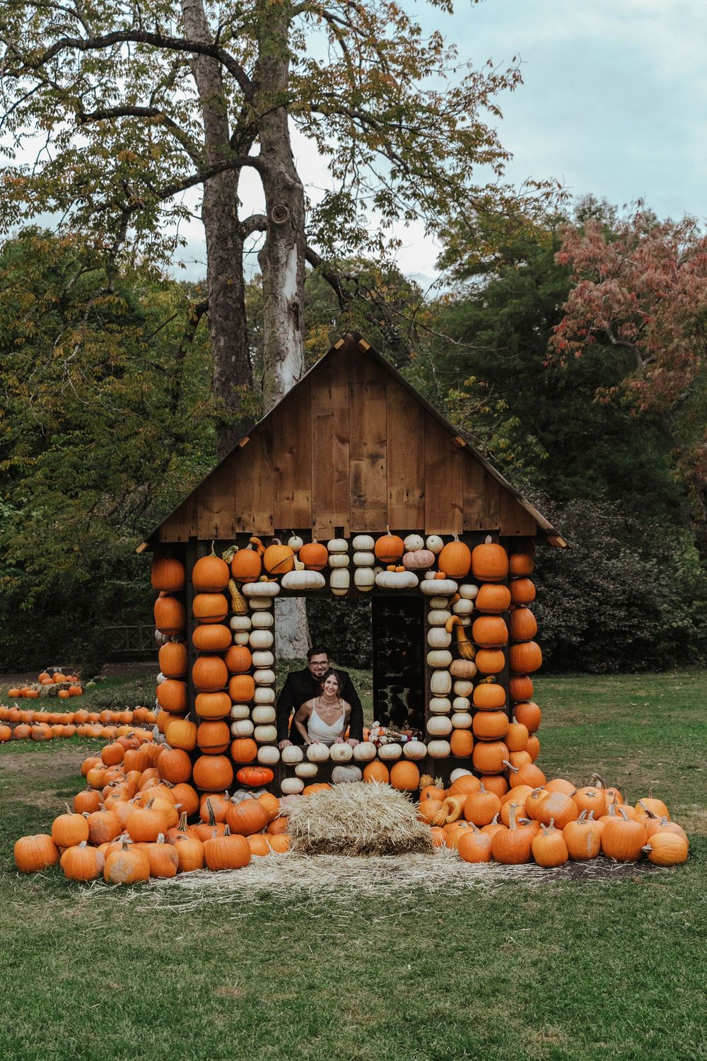 A rustic wooden structure decorated with numerous orange pumpkins and hay bales for fall season display in an outdoor setting.