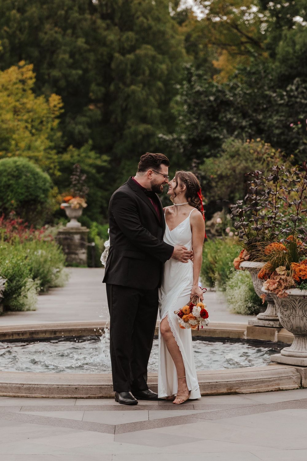 Two people in a romantic moment share a series of tender poses on stone steps surrounded by autumn foliage in a garden setting.