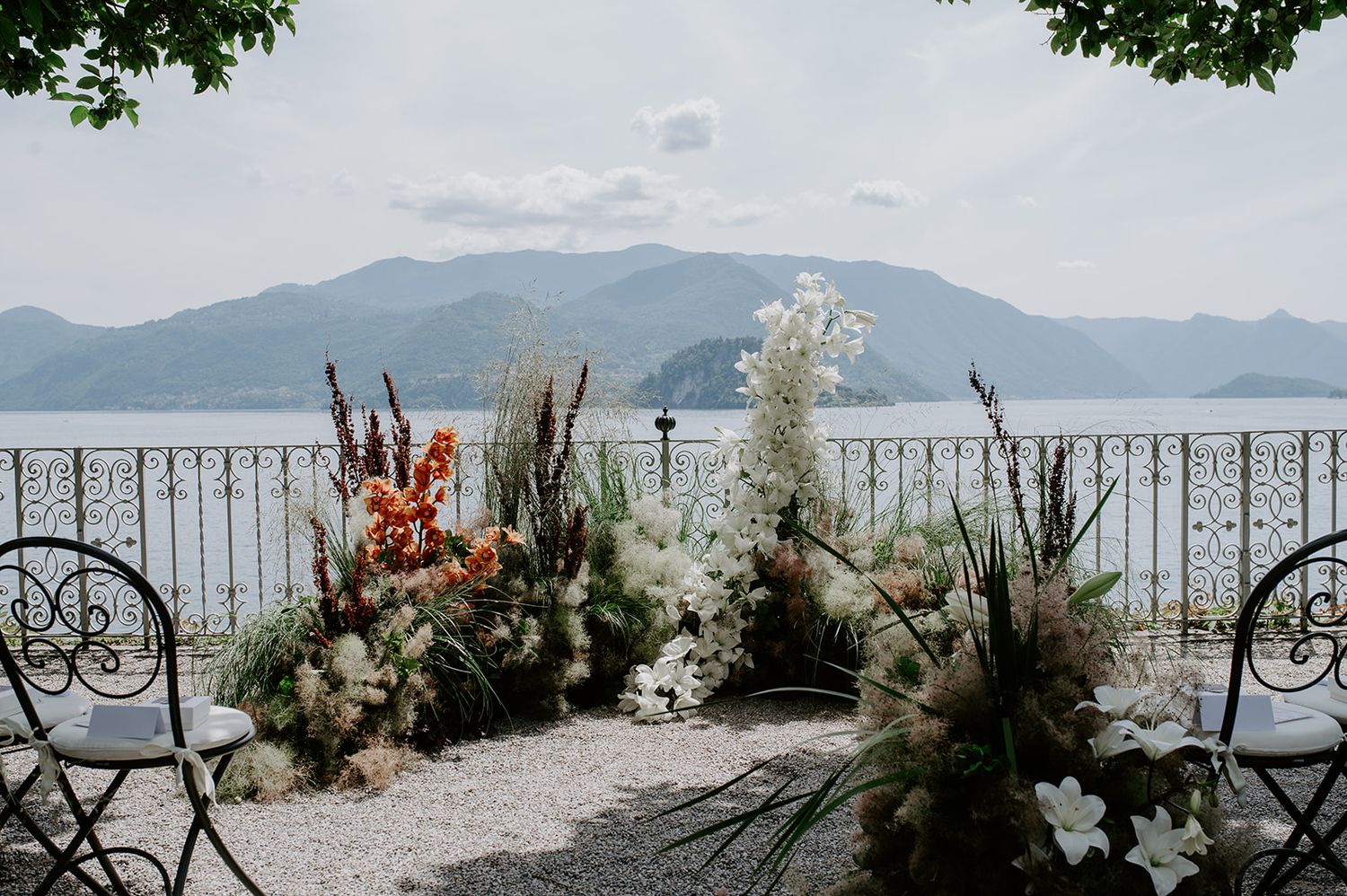 Scenic lakeside wedding ceremony setup with elegant white floral arrangements and mountains in the background.