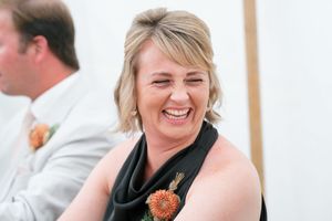 A candid moment at a celebration shows a joyful guest wearing a black top with an orange floral accent.