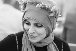 Black and white portrait of person in a headscarf and floral crown looking down with a gentle smile.