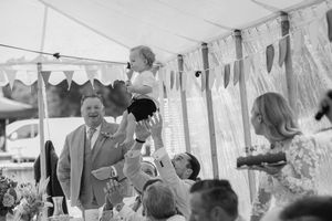 A celebratory scene at an outdoor event with attendees gathered under a white tent during what appears to be a reception.