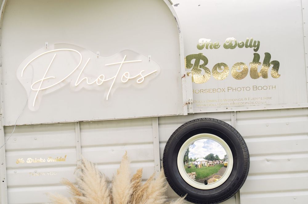 A vintage photo booth exterior with neon 'Photos' signage and a circular window decorated with pampas grass.