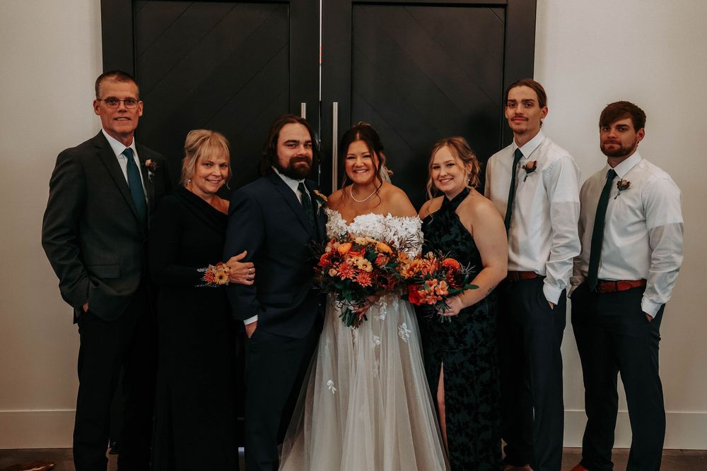 Wedding party members in formal attire stand together in a dimly lit venue creating an elegant atmosphere.