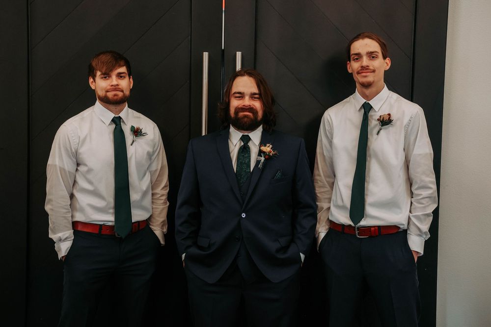 Professional group photo of groomsmen in formal attire posing against a dark wall.