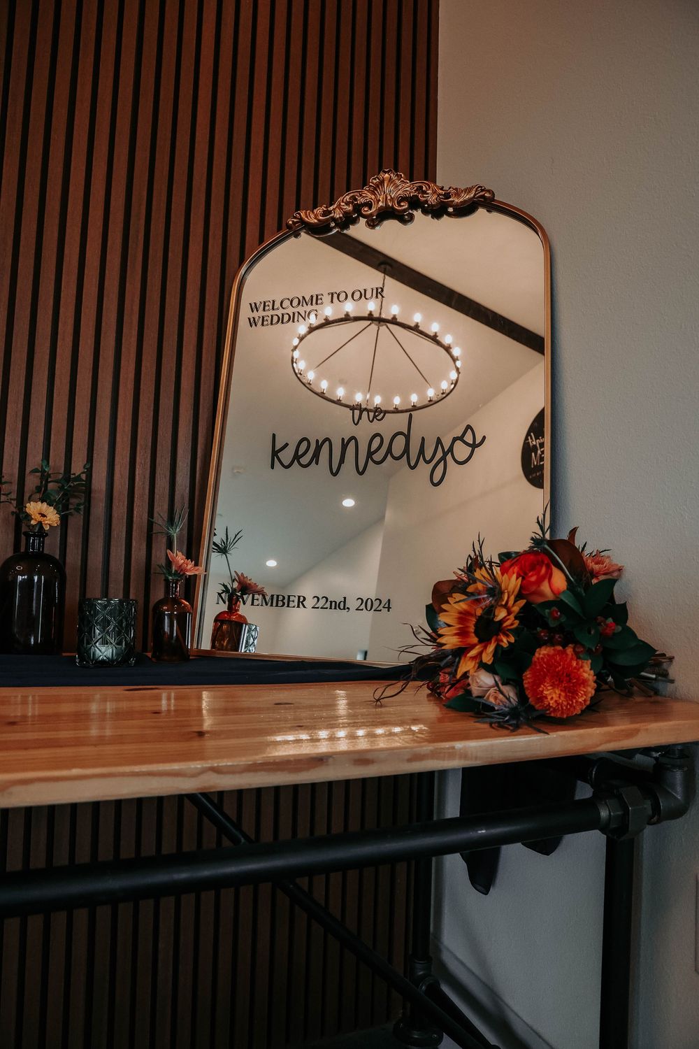 Decorative wedding mirror with text and floral arrangements features wood paneling backdrop and warm lighting ambiance.