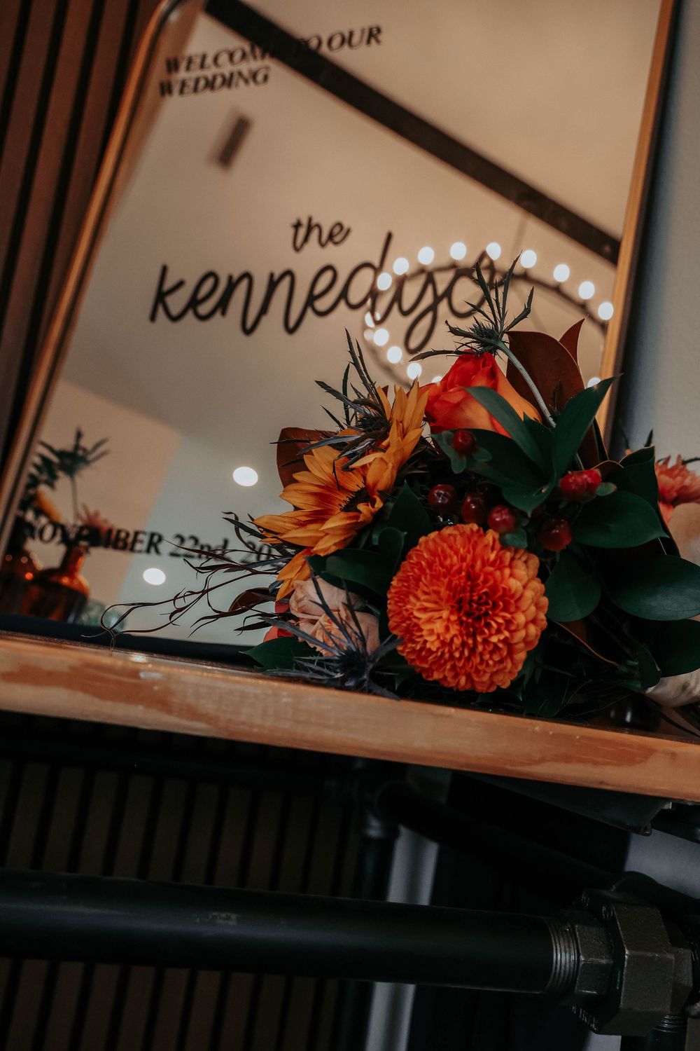 Close-up details of wedding stationery with fall-themed floral arrangements featuring orange dahlias and dark greenery.