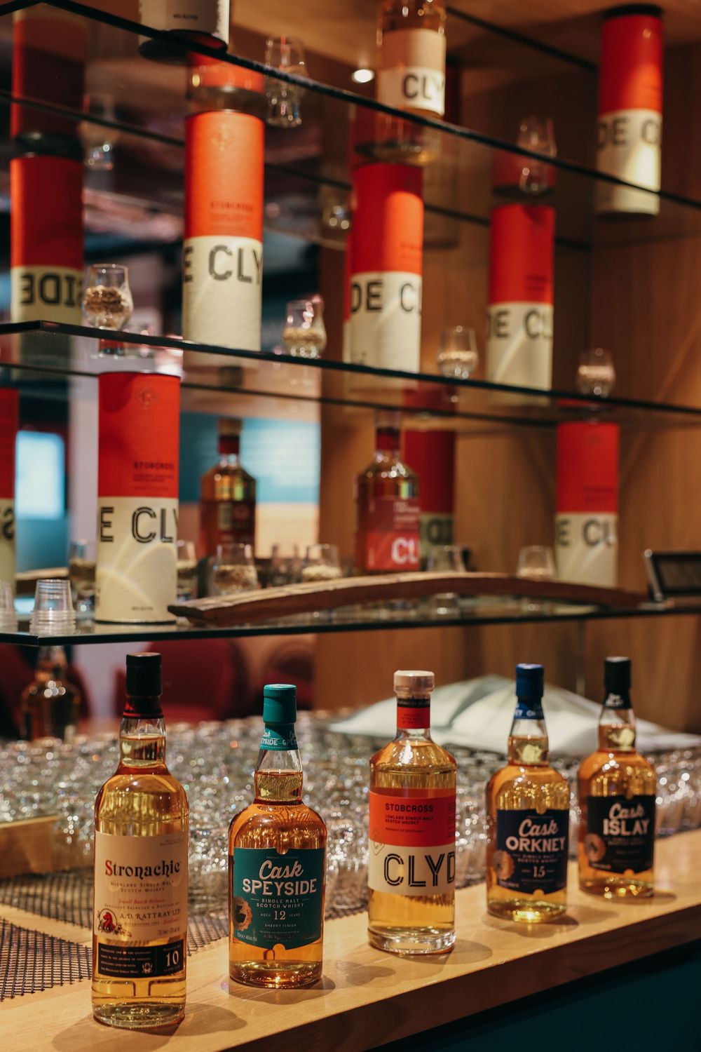 Array of whiskey bottles displayed on illuminated glass shelves in a high-end bar setting.