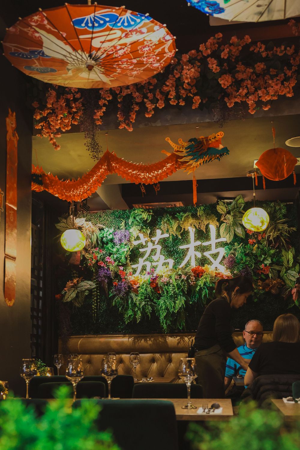 Asian restaurant decor with paper lanterns, dragon decorations, and neon signs among artificial foliage.