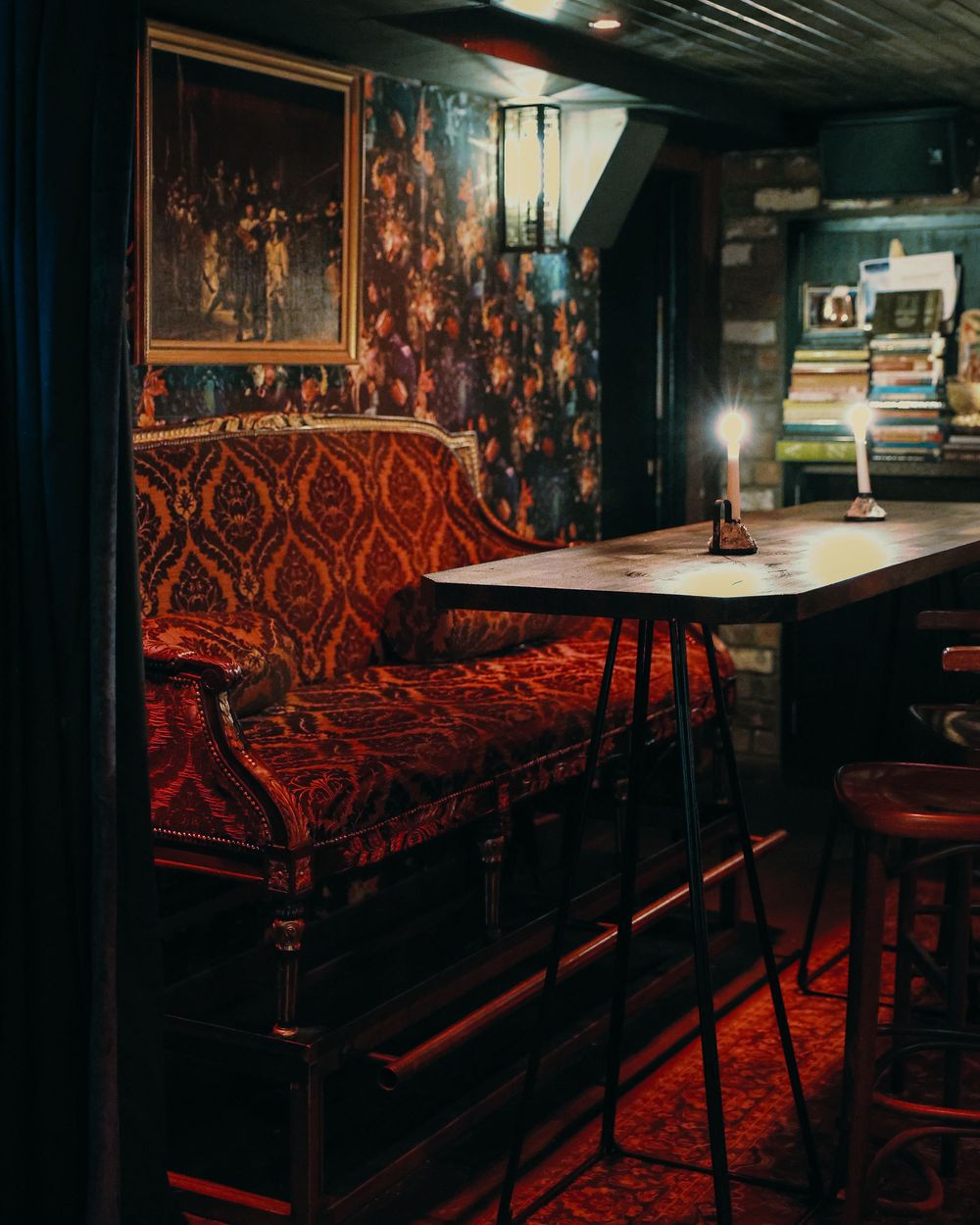 Dark bar interior with red upholstered bench seating and vintage artwork on walls.