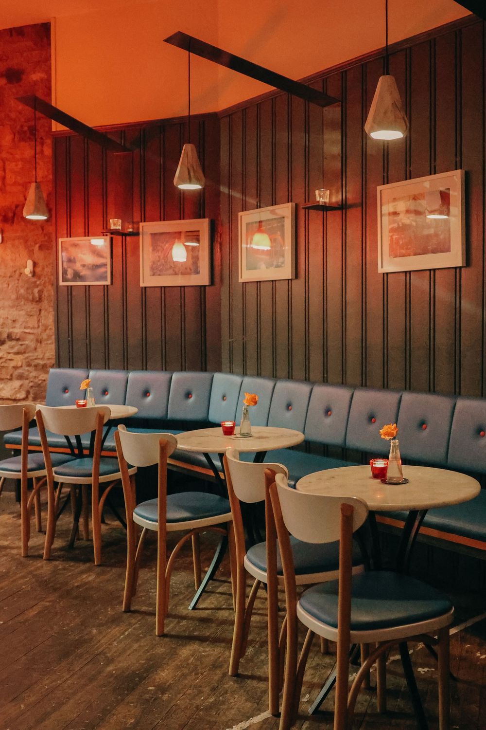 Retro diner interior with blue tufted banquette seating and round tables under pendant lights.