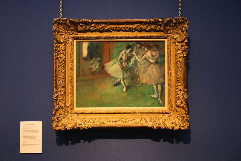 Gold-framed ballet painting illuminated in a dark museum gallery.