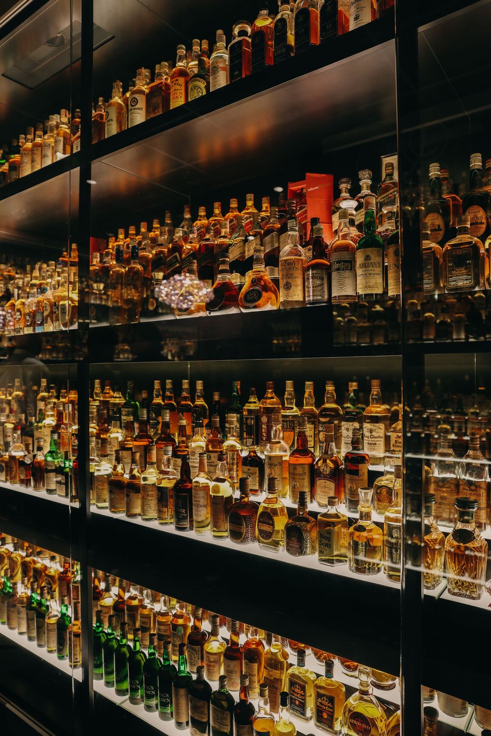 Illuminated shelves displaying an extensive collection of whiskey bottles in a dark bar setting.