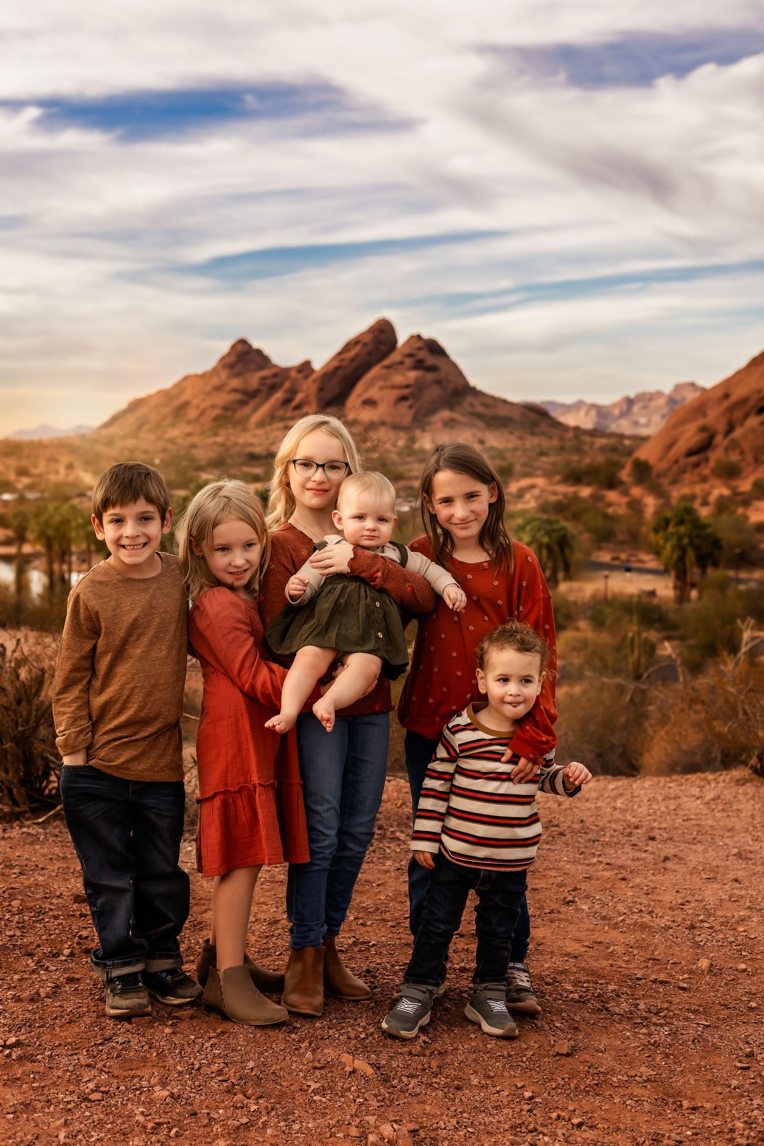 Desert landscape panorama with majestic red rock formations in the background and children sitting on desert terrain during sunset.