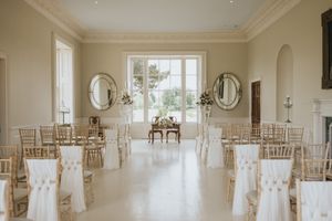 Elegant wedding ceremony room with white chairs, oval mirrors, and large windows in a bright interior space.