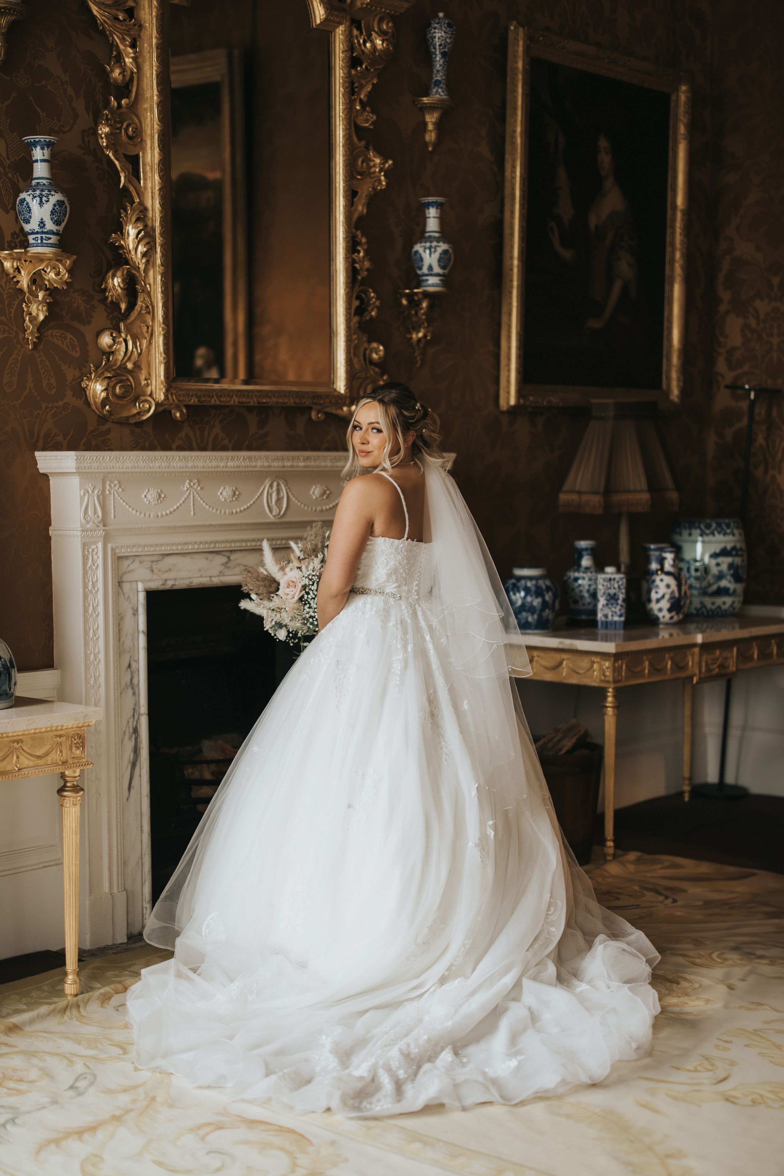 Elegant white wedding dress train flowing across ornate floor in luxurious historic room with gilded details.