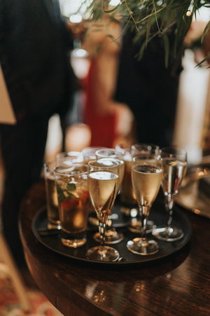 Several champagne glasses and cocktails sit on a dark wooden surface at a party or celebration.