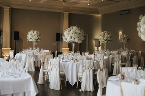 Elegant wedding reception venue with white linens and floral centerpieces on round tables set for a celebratory dinner.