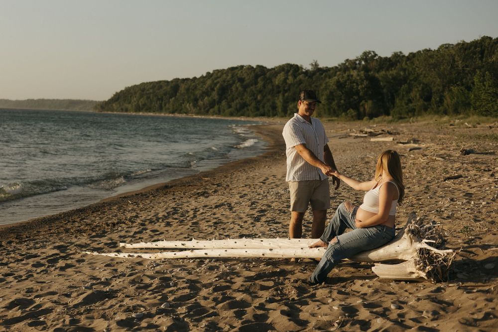 Two people share a romantic moment on a beach at sunset with a surfboard and blanket laid out on the sandy shore.