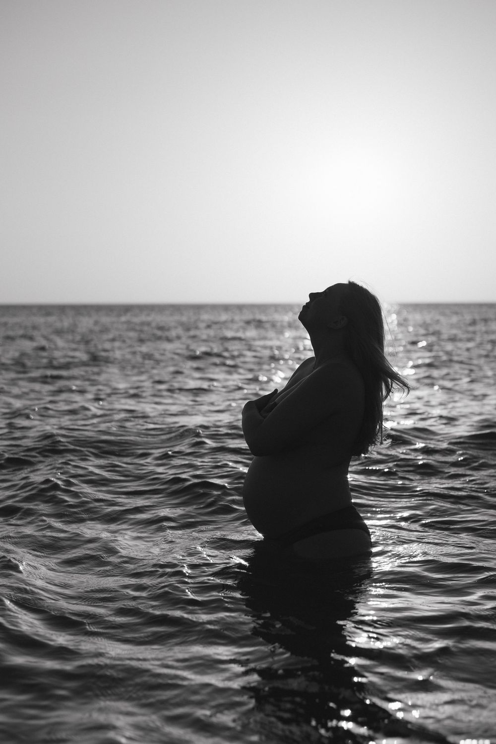 A black and white series of silhouettes shows a figure emerging from dark ocean waters against a bright horizon.