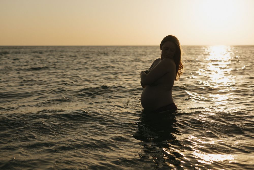 Silhouette of a person swimming in the ocean at sunset with sparkling golden water reflections on the surface.