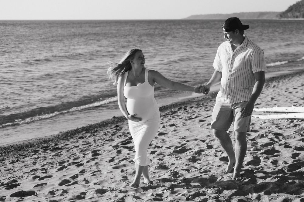 A couple walks together along a scenic beach shoreline at sunset, leaving footprints in the sand.