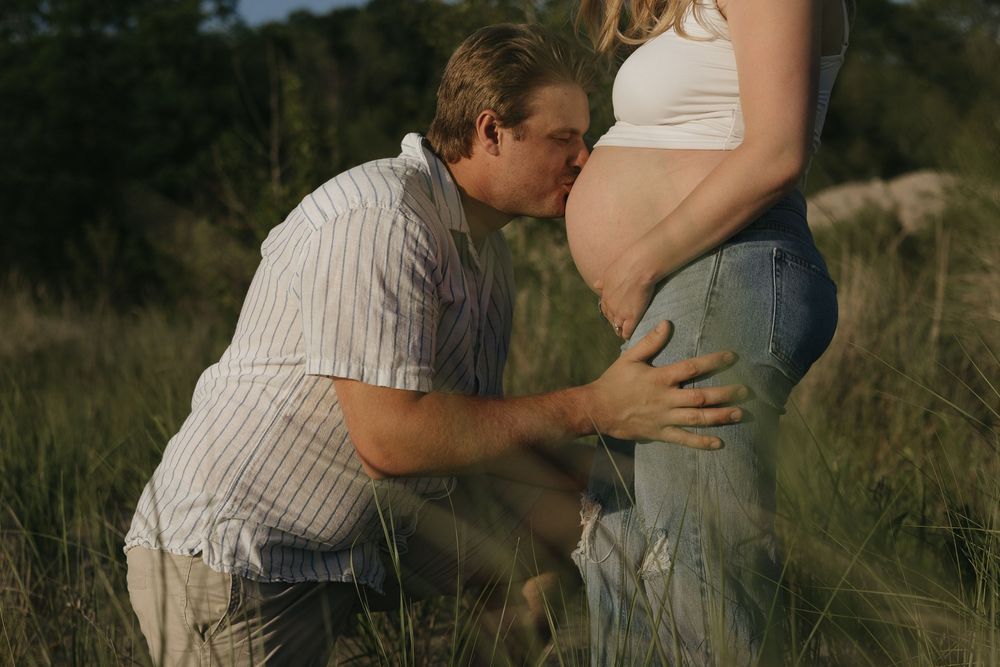 A tender moment with an expecting couple in a grassy field at sunset.