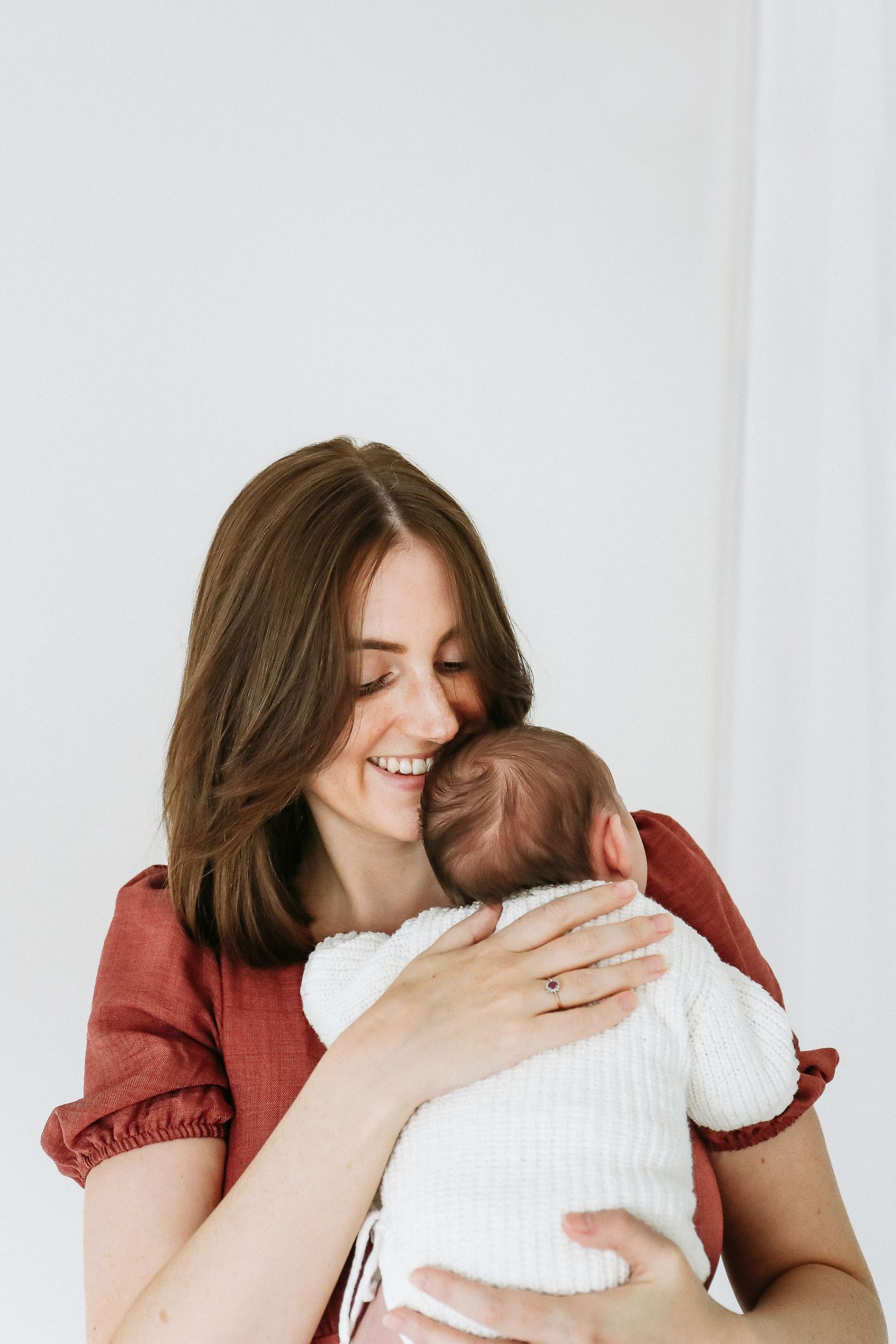Photo showing mum in a red dress hugging and embracing her newborn,  during newborn photoshoot in Nottingham