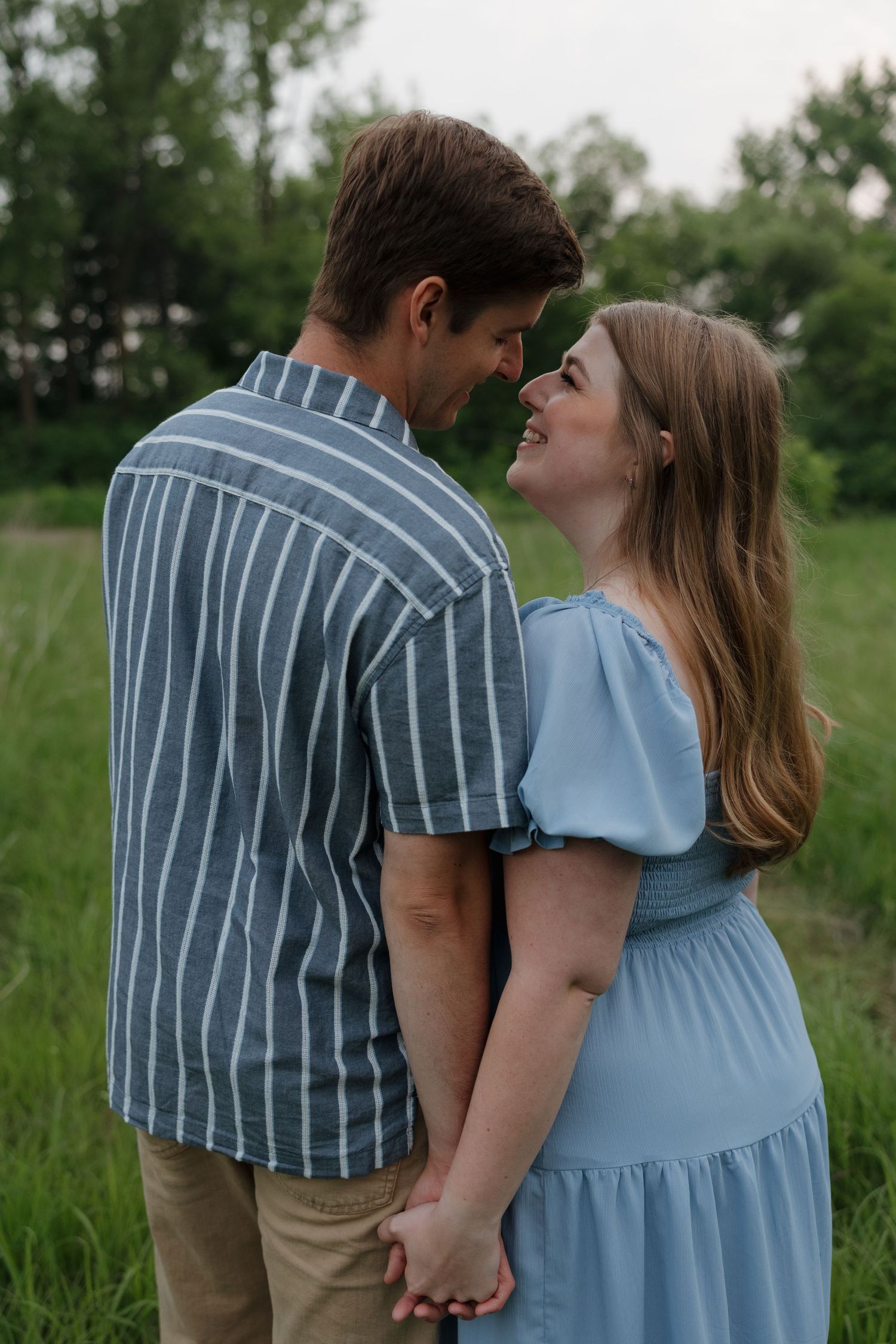 Two people in a romantic embrace share an intimate moment in a grassy field on a summer day.