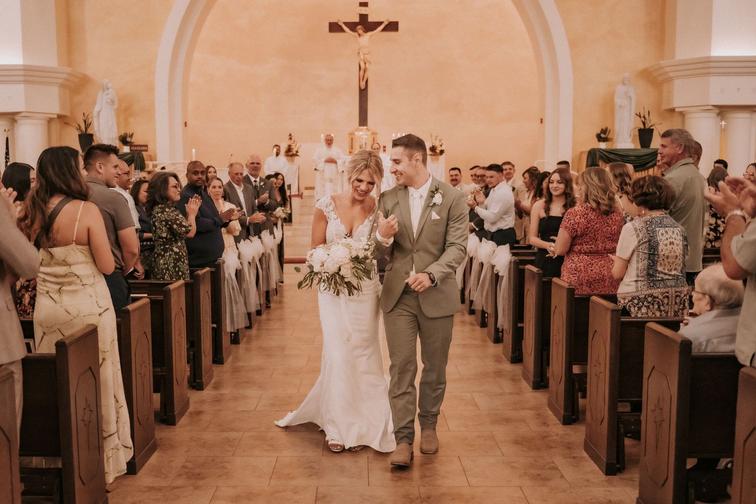 A newly married couple walks down the church aisle together as guests look from wooden pews. Affordable wedding photographers in New Mexico