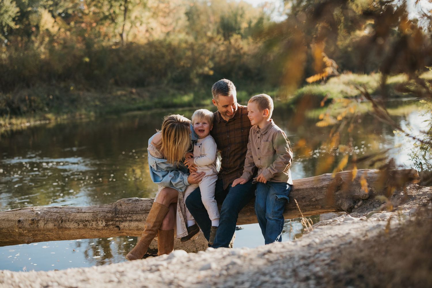 A loving family huddles together on a peaceful riverbank during a golden autumn afternoon.
