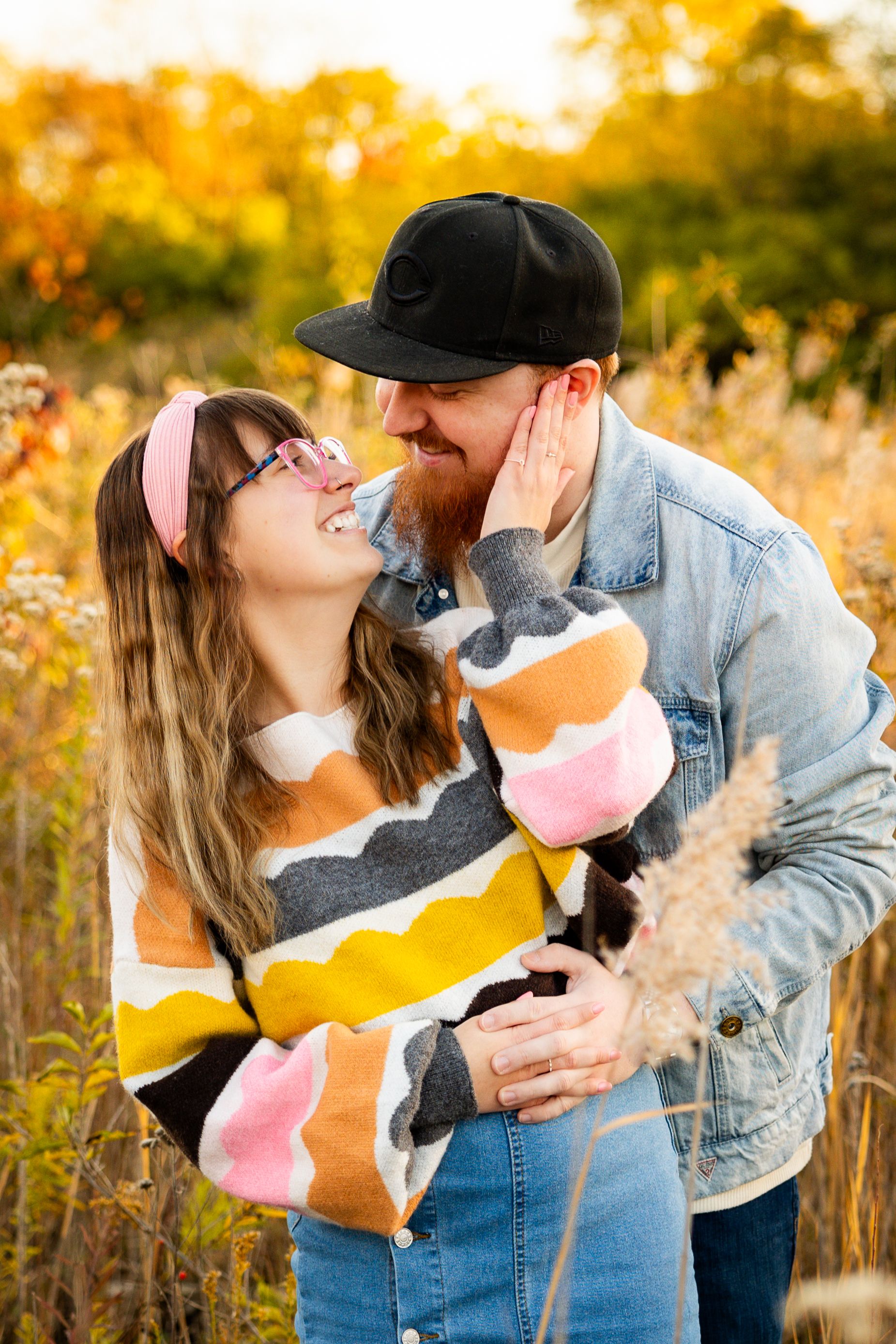 A couple shares a tender moment with their dog in a golden autumn field at sunset.
