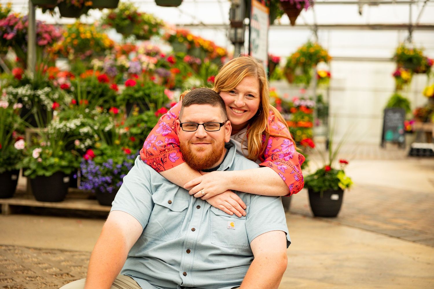 Two people sharing a warm embrace in a garden center surrounded by colorful flowers and hanging baskets.