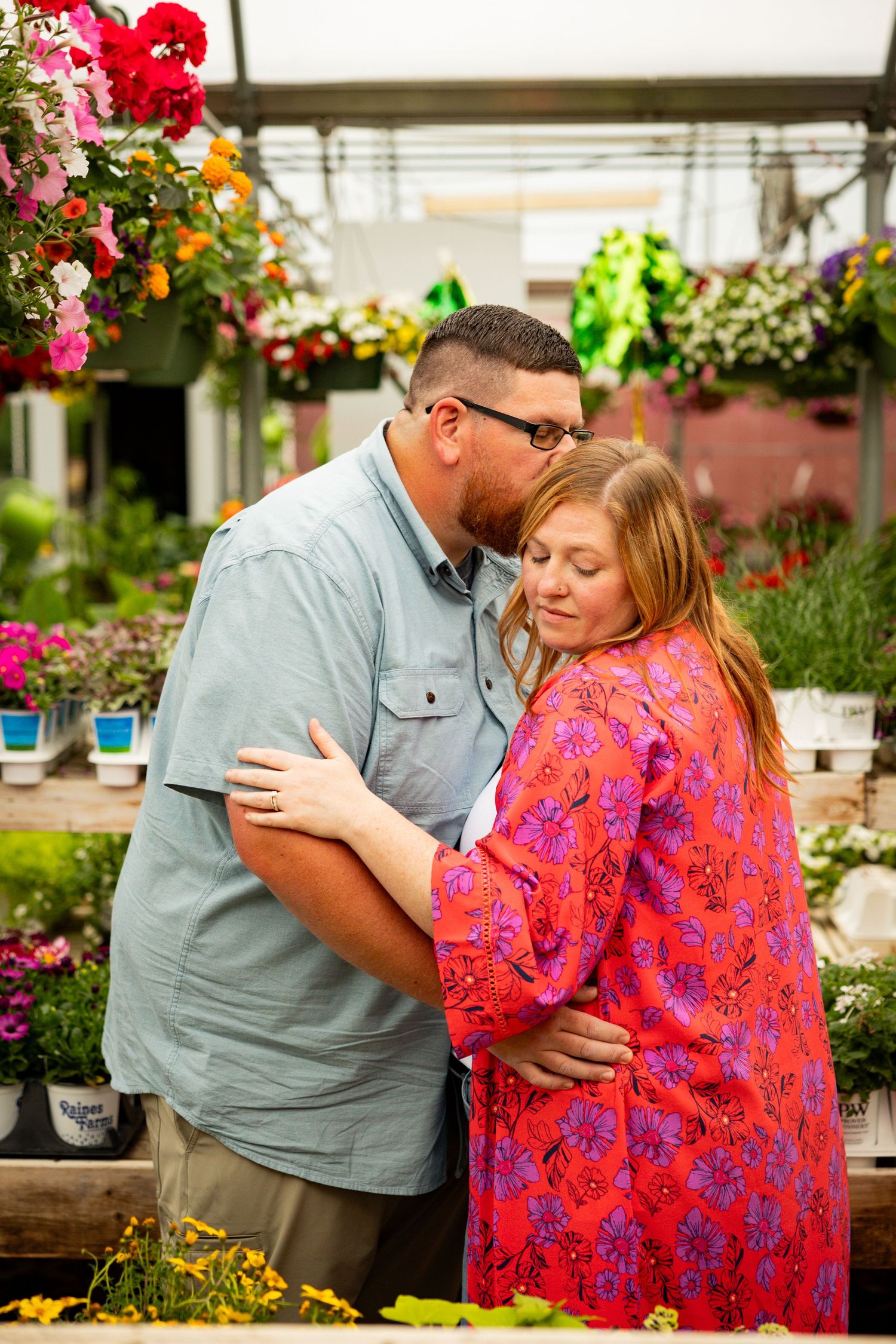 A couple shares intimate moments in a garden nursery setting with vibrant flowers and greenery.