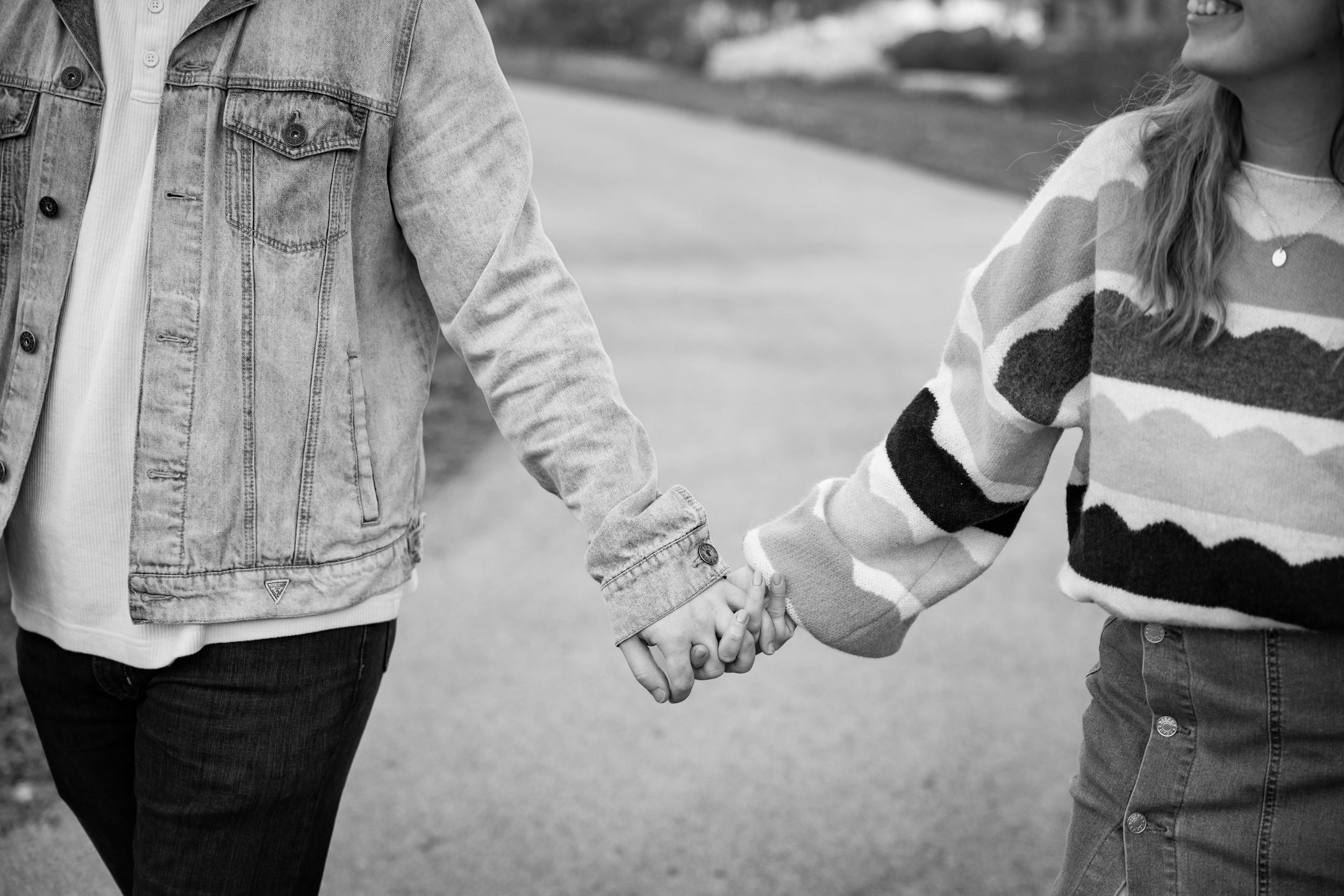 Two people hold hands while walking together on a sidewalk in a black and white photograph.