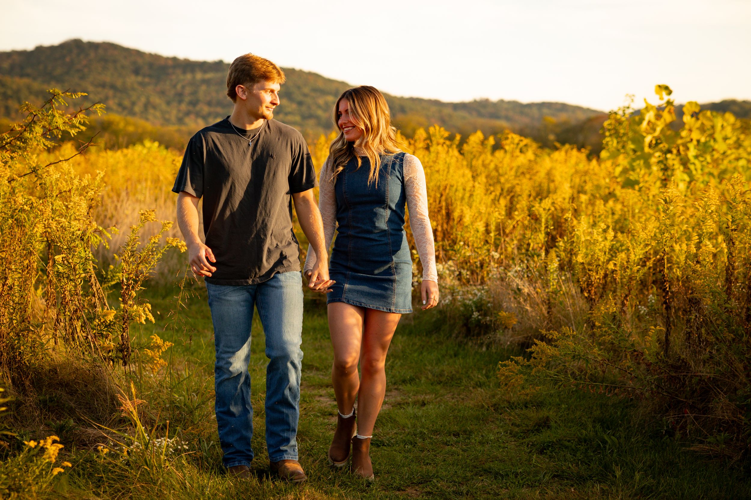 Couple walking hand in hand through a golden field at sunset creating silhouettes against the warm glowing sky.