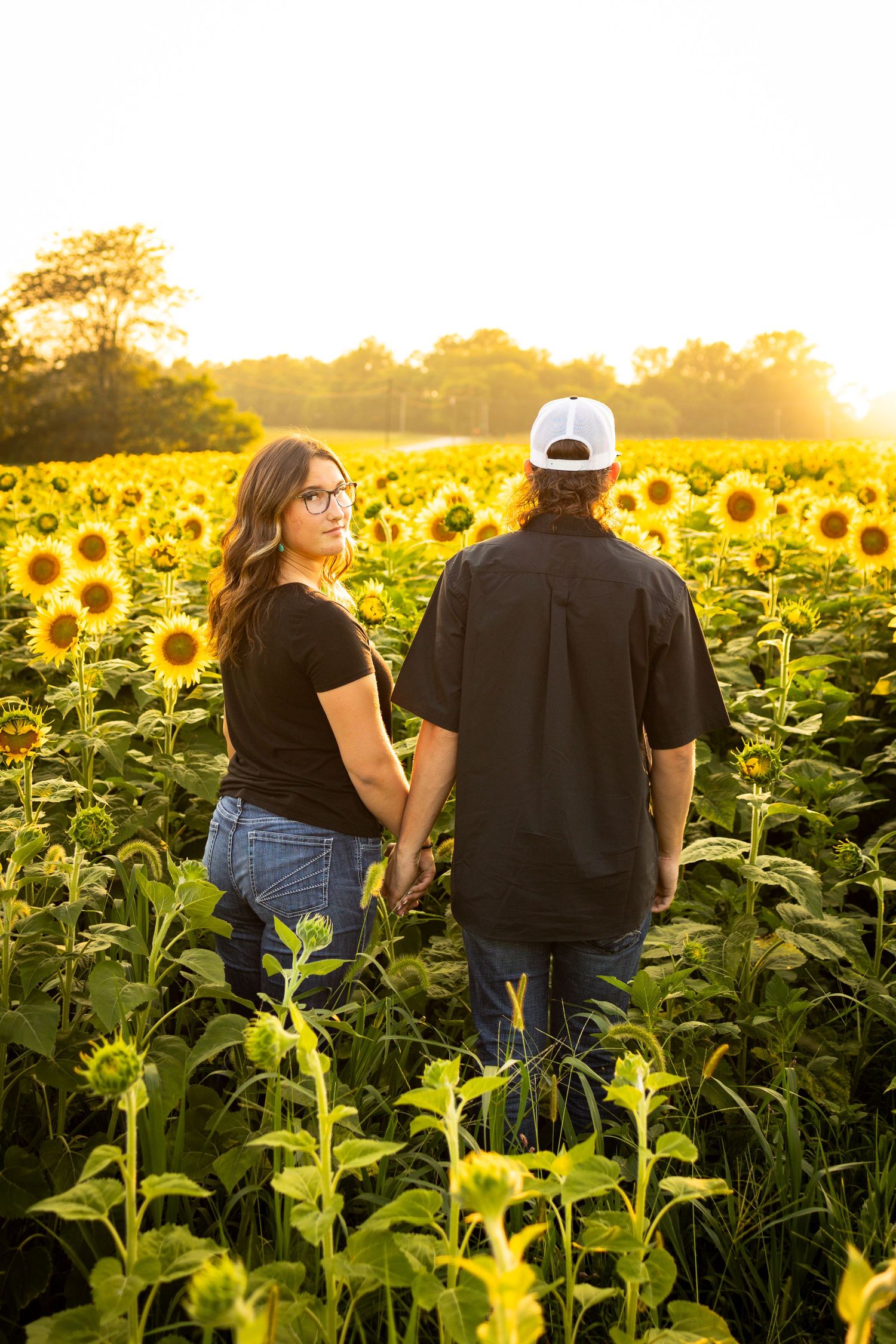 Two people share an intimate moment at sunset in a vibrant field of blooming sunflowers.