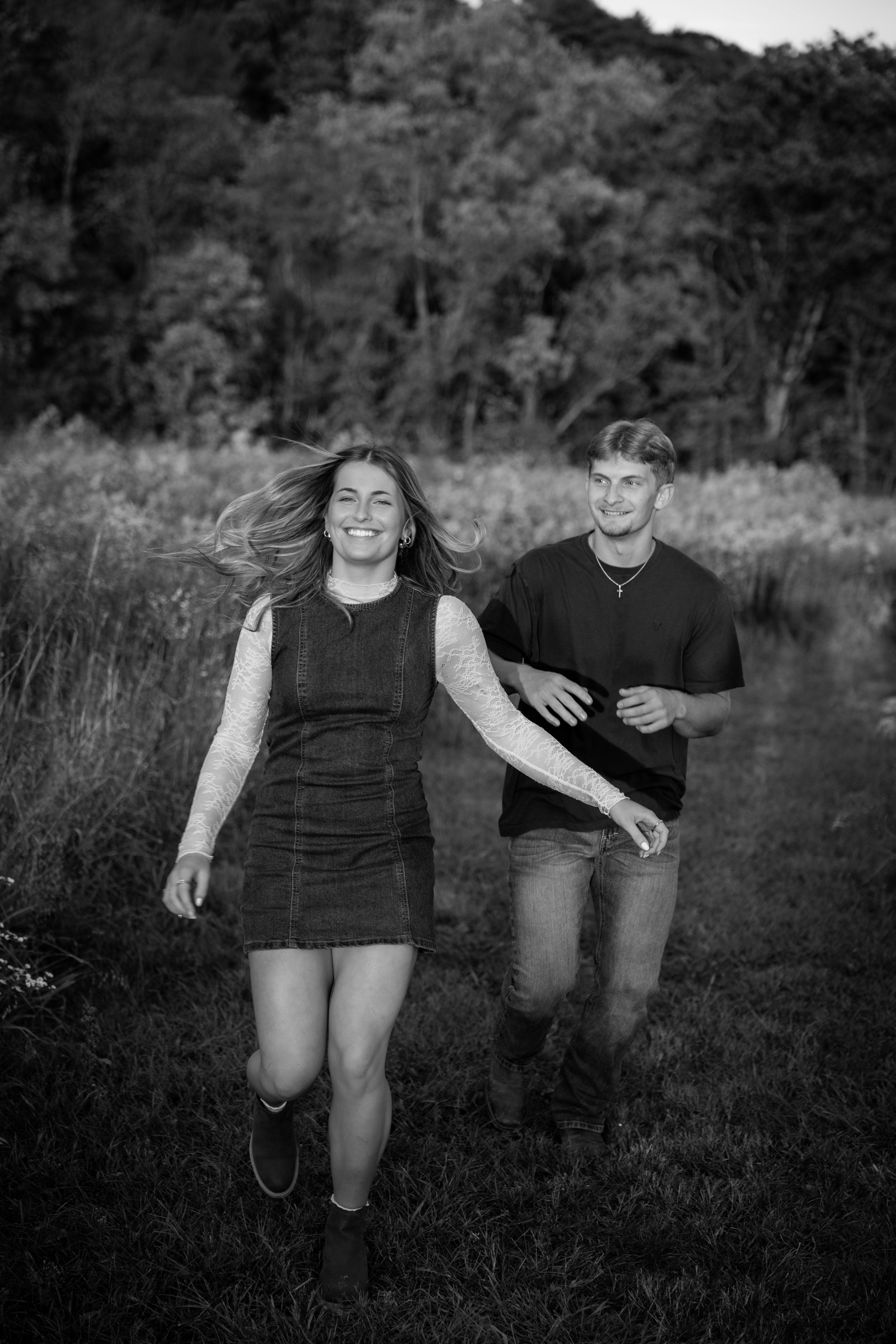 Black and white photo of a couple running and laughing together through a meadow.