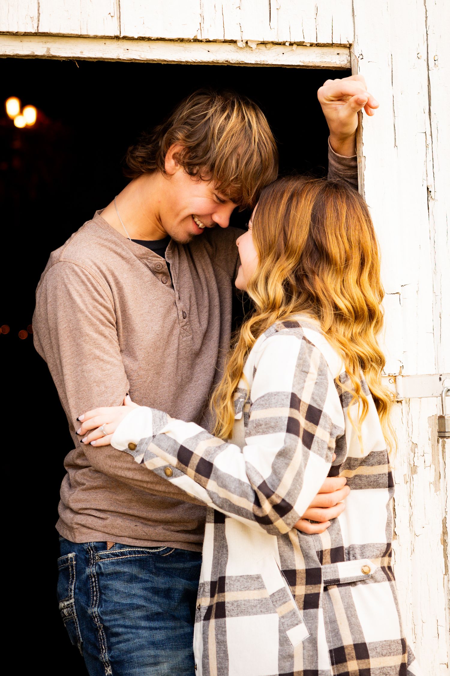 A young couple shares an intimate moment in front of a rustic barn door wearing casual autumn attire.