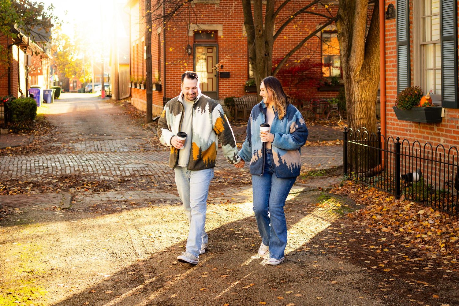 Two students walk together on a brick sidewalk during autumn with golden sunlight streaming through trees on a historic campus.