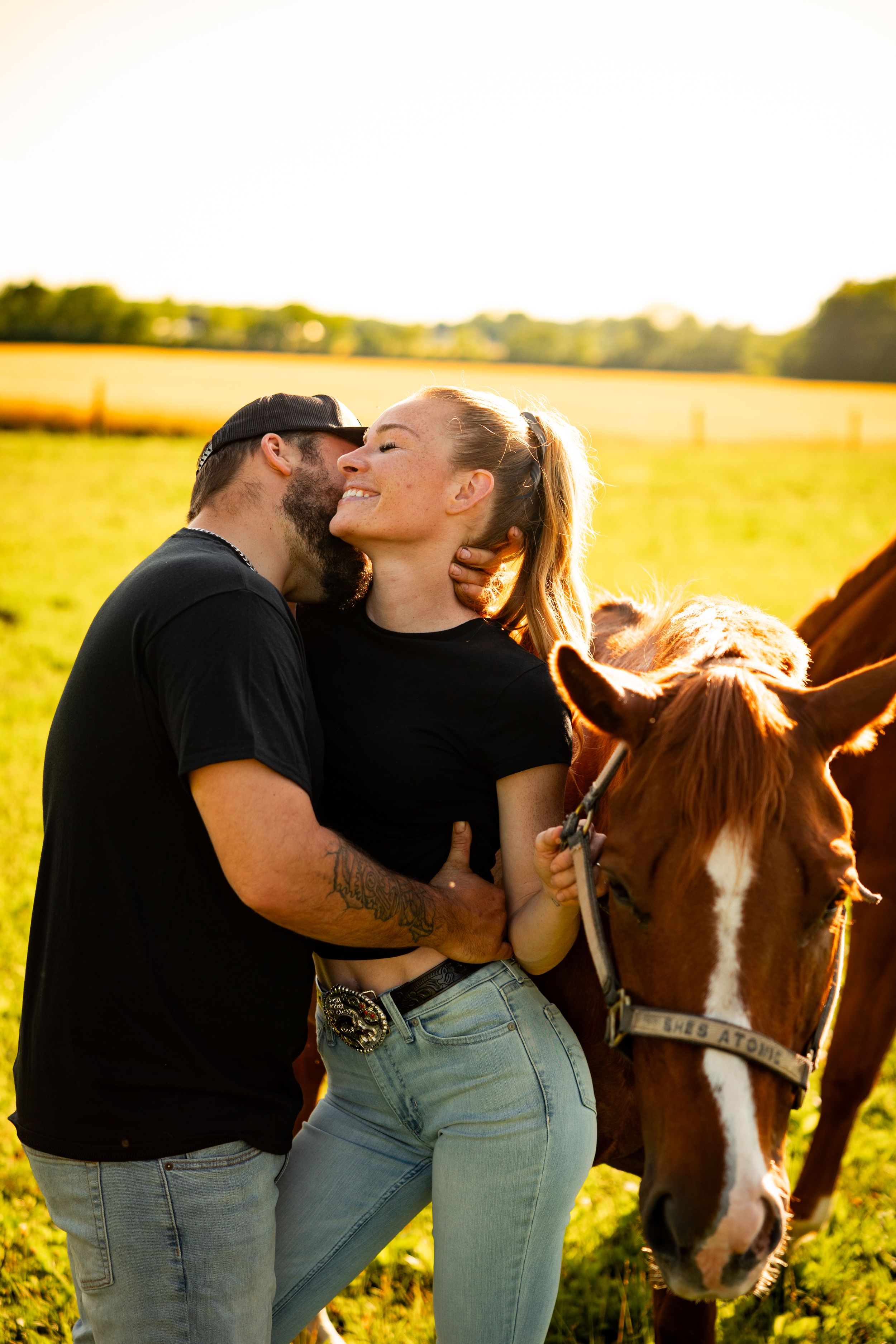 A romantic couple shares tender moments with their horse in a sunlit field at golden hour.