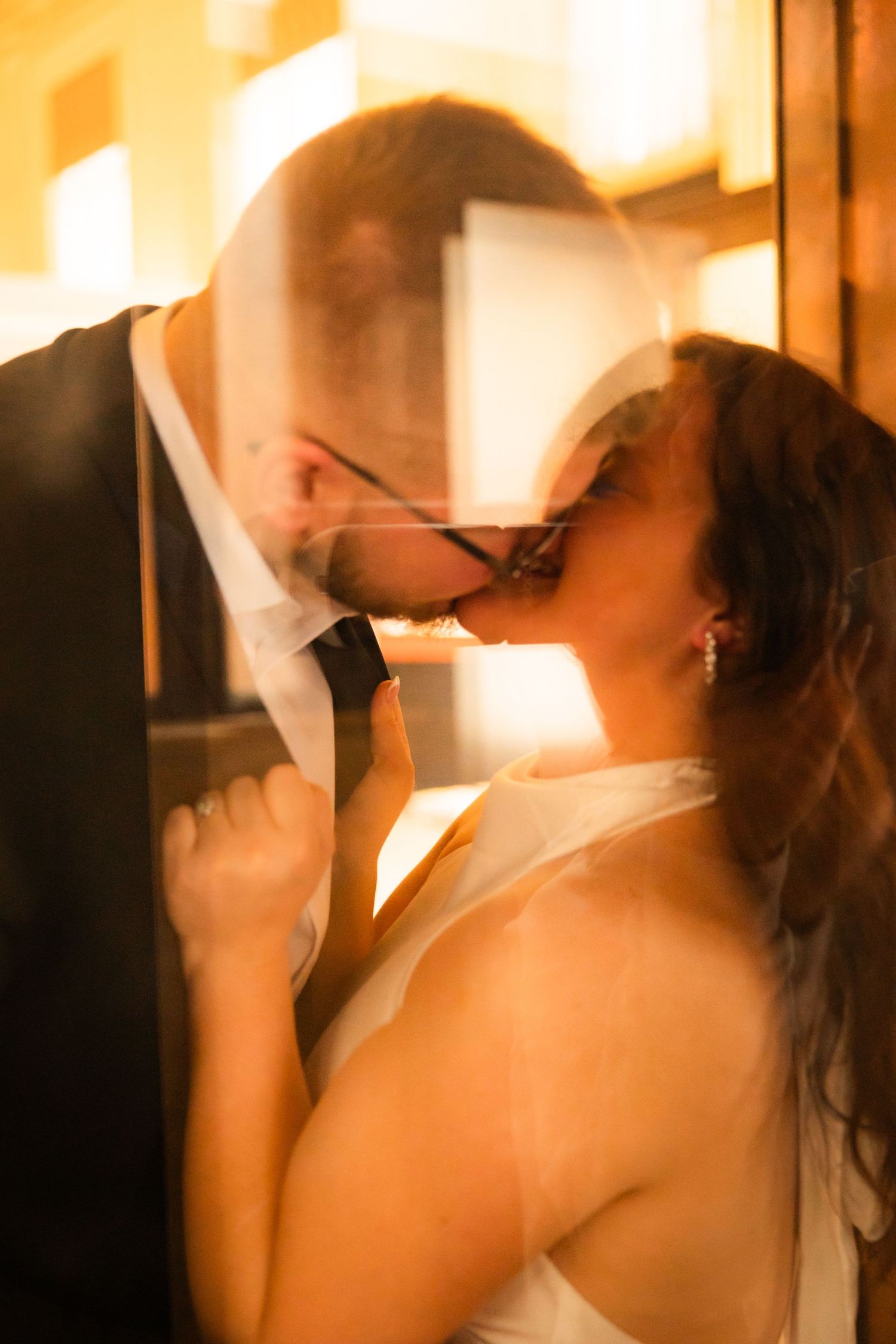 Romantic wedding couple shares an intimate kiss in soft golden lighting during their reception celebration.