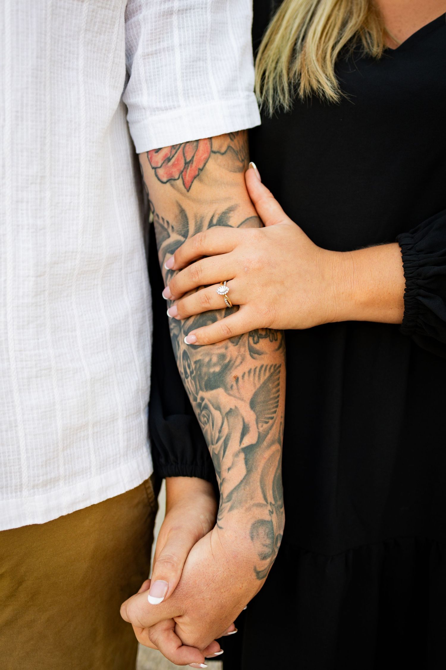 Hand with intricate sleeve tattoo being held by another person wearing a black top and diamond engagement ring.